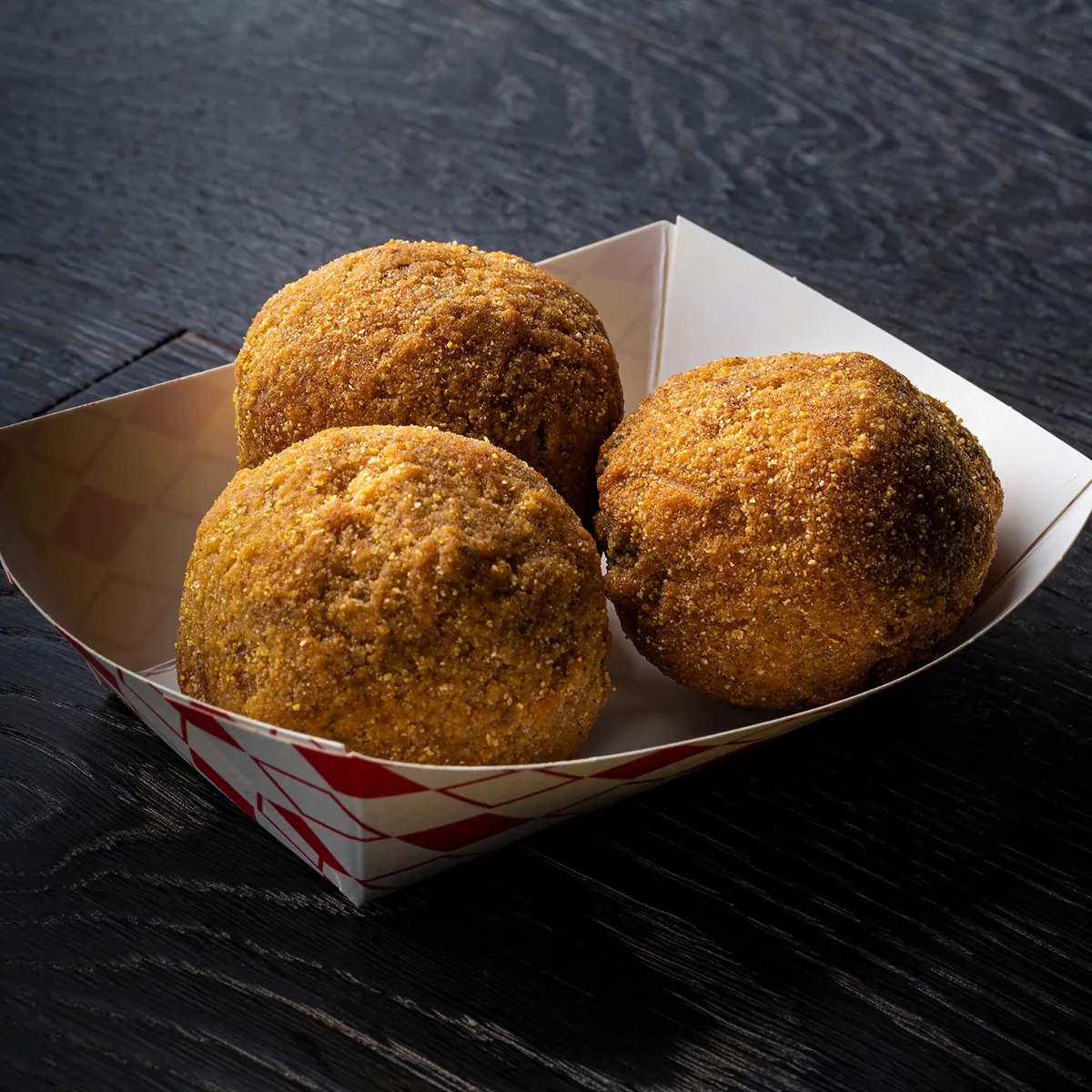 Three golden fried boudin balls in a paper tray