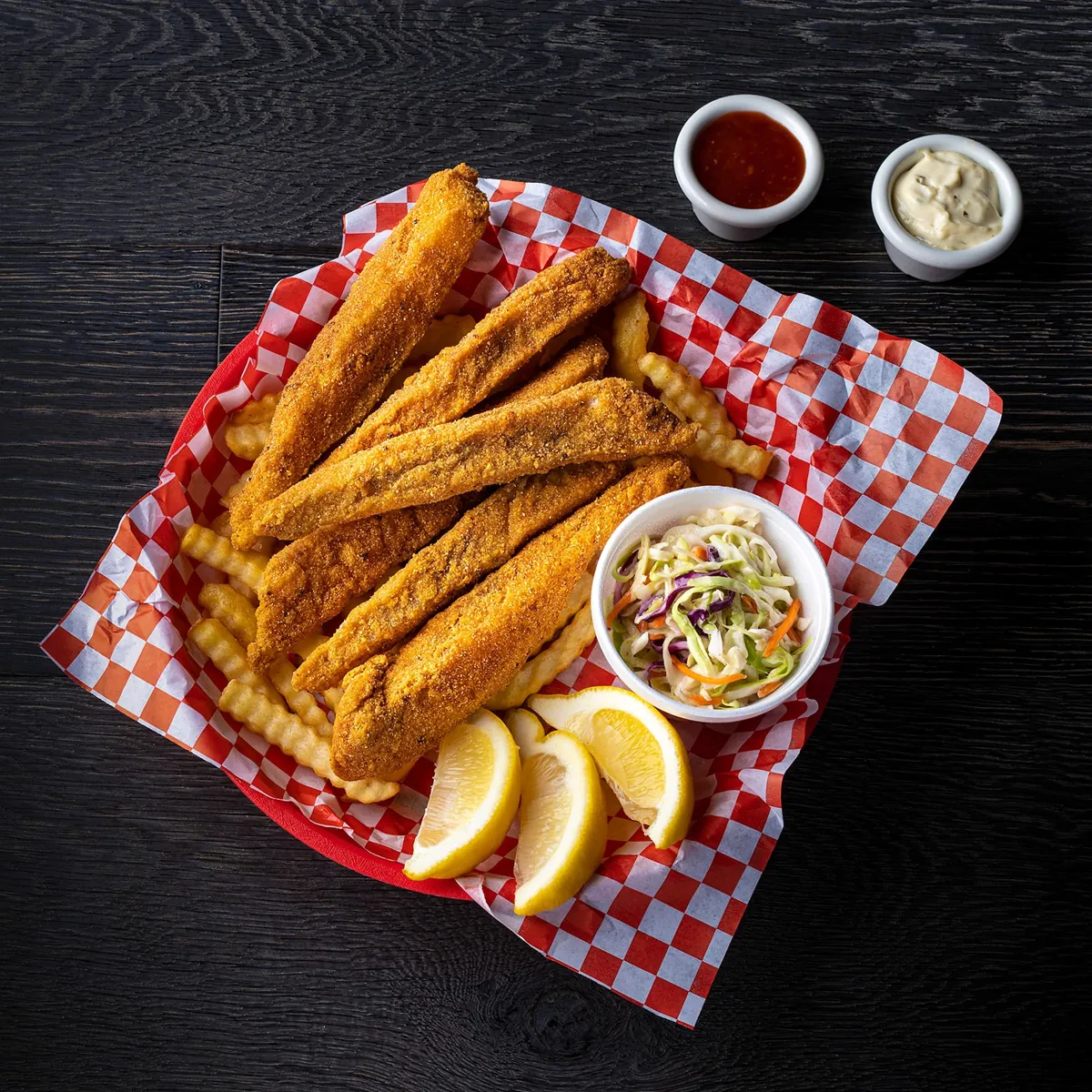 Fried catfish strips with crinkle fries, cole slaw and lemon in a red-checkered basket