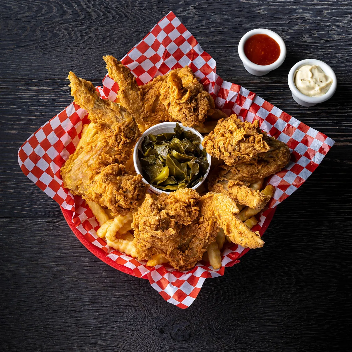Fried chicken wings and fries around a bowl of collard greens